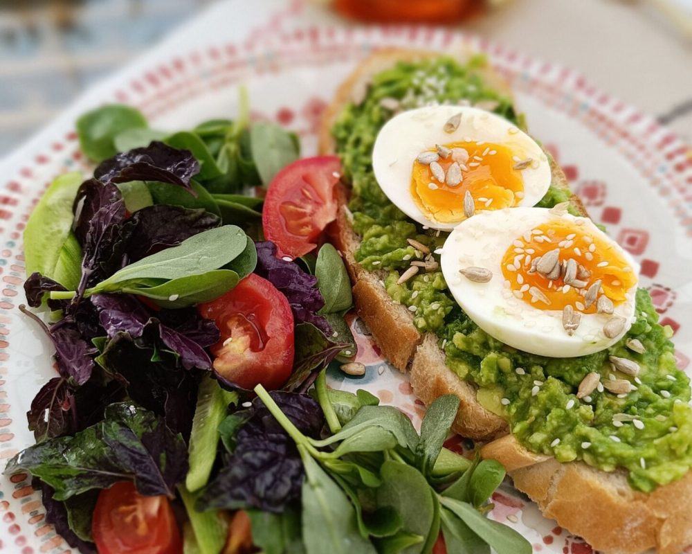 Delicious avocado toast topped with eggs and a fresh salad.